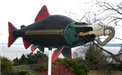 Large spinning sculpture of a salmon with a gas mask on its face titled 