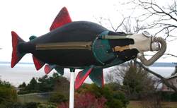 Large spinning sculpture of a salmon with a gas mask on its face titled 